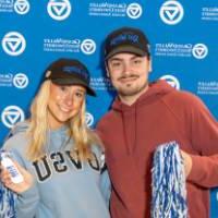 Two alums holding pom poms by the Alumni Relations backdrop